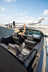 Woman In Convertible Waving To Pilot And Stewardess Against Jet - obrazy, fototapety, plakaty