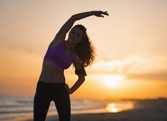 Silhouette of fitness young woman stretching on beach at dusk