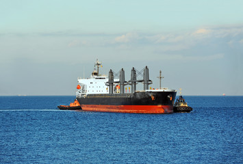 Tugboat assisting bulk cargo ship to harbor quayside