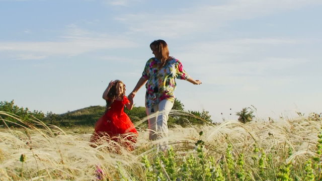 Mother and daughter running across summer field. Slow motion