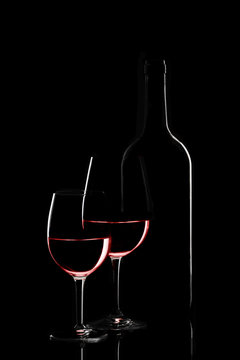 Red wine bottle and two wine glasses on black background on blac