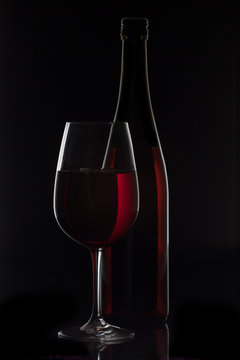 Red wine bottle and wine glass on black background