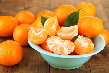 Ripe tangerines in bowl on wooden background