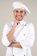 Professional chef in white uniform and hat, on gray background