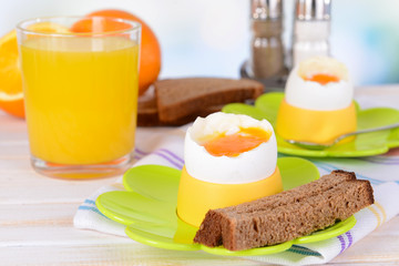 Boiled eggs in egg cups on table on light background