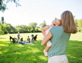 Mother Carrying Cheerful Daughter In Park