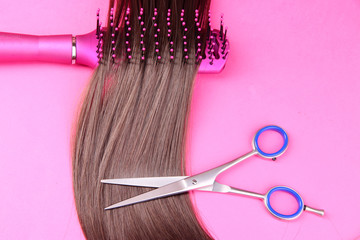 Long brown hair with hairbrush and scissors on pink background
