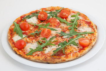 Pizza with tomato and arugula on white plate