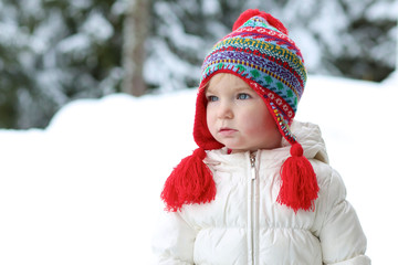 Pretty toddler girl in beautiful warm outfit plays in snow