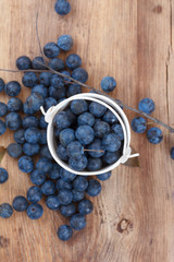 Blackthorn berries on wooden table, focus on berries in pail