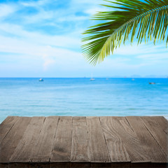 Empty wooden table with tropical sea and palm leaf on background
