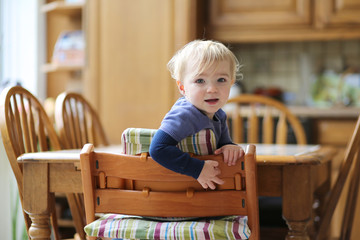 Portrait of smiling blonde toddler girl sitting in the kitchen 