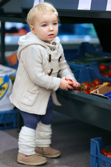 Adorable blonde toddler girl picking up tomato from a shelf