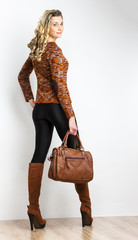 standing woman wearing fashionable brown boots with a handbag