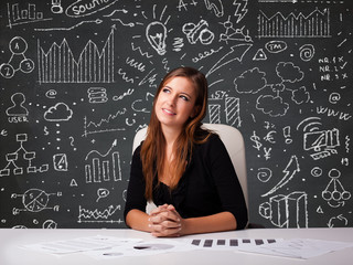 Businesswoman sitting at desk with business scheme and icons