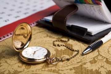 Fototapeta na wymiar Gold pocket watch and a wall calendar and sketchpad