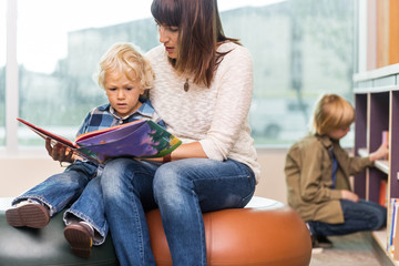 Teacher With Boy Reading Book In Library