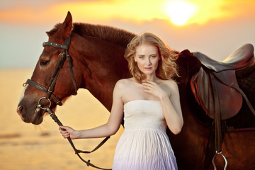 Beautiful woman riding a horse at sunset on the beach. Young gir