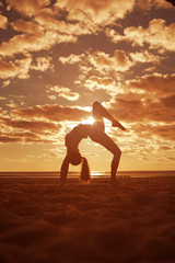 Fototapeta na wymiar Young beautiful slim woman silhouette practices yoga on the beac