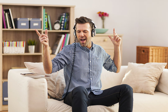 Handsome young man sitting on his sofa and listening to music .