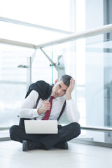 Stressed out businessman seated on floor working at laptop