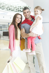 Father and mother pose with young daughter in shopping mall