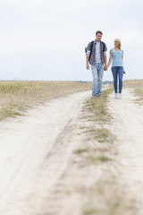 Full length of young hiking couple walking on trail at field