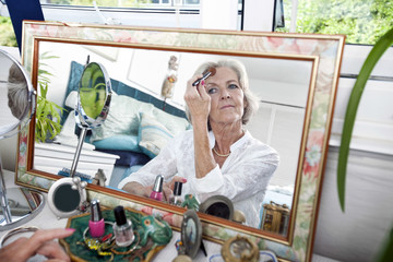 Mirror reflection of senior woman applying blusher at home