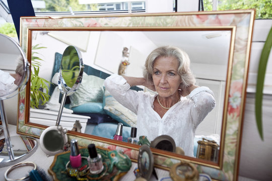 Mirror Reflection Of Senior Woman Putting On Necklace At Home