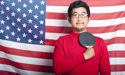 Proud Asian Man holding table tennis paddle against US Flag