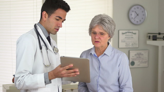 Hispanic doctor talking to mature woman with tablet computer