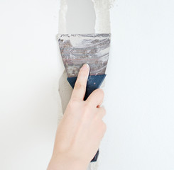 Female hand repairs wall with spackling paste