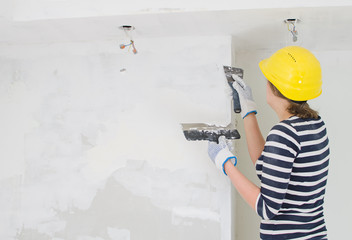 Female plasterer repairs wall with spackling paste.