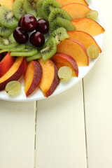 Assortment of sliced fruits on plate, on white wooden table