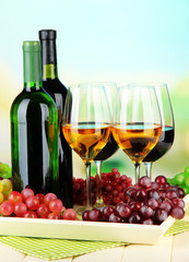 Wine bottles and glasses of wine on tray, on bright background