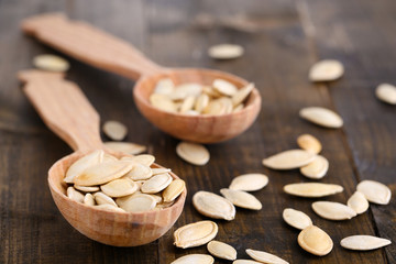 Pumpkin seeds in spoons on wooden background