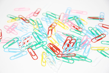 Pile of many multicolored plastic paper clips on white paper.