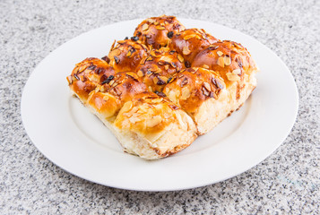 Homemade sweet bun with almond and raisins on a white plate