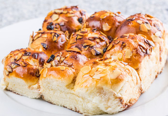 Homemade sweet bun with almond and raisins on a white plate