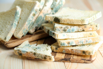 Mouldy bread on cutting board, on wooden background