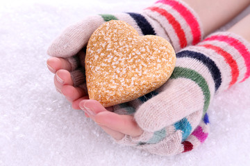 Female hands in mittens with heart on snow background