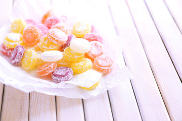 Sweet  multicolor candies on paper, on  color wooden background