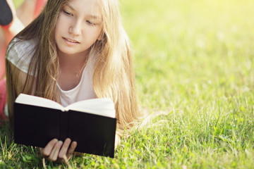 young teenage girl reading book on grass