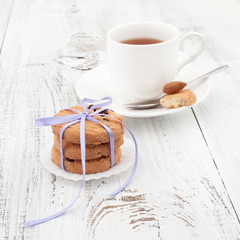 Chocolate chip cookies on a white plate with cup of tea