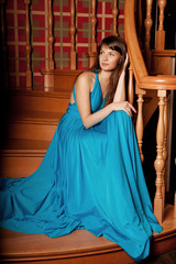 Beautiful woman in a long blue dress in the rich interior. Young