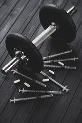 Dumbbell, syringes and tablets on a dark wooden surface