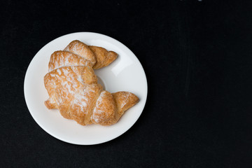 fresh croissant on a plate on black background, top view