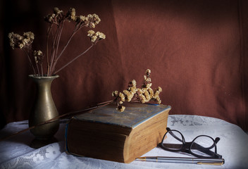 Still life metal vase flower with antique book and eyeglasses.