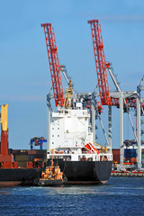Fototapeta premium Tugboat assisting container cargo ship to harbor quayside