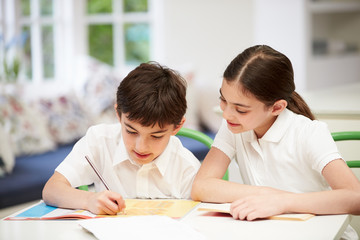 Children Wearing School Uniform Doing Homework In Kitchen